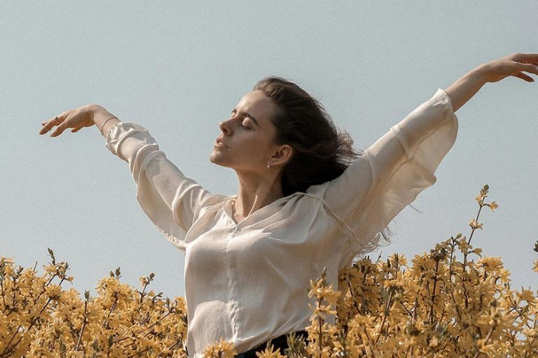 dependencia_emocional_sensacion_coaching_oscar_madrid Mujer respirando relajada con los brazos abiertos rodeada de muchas flores blancas y amarillas